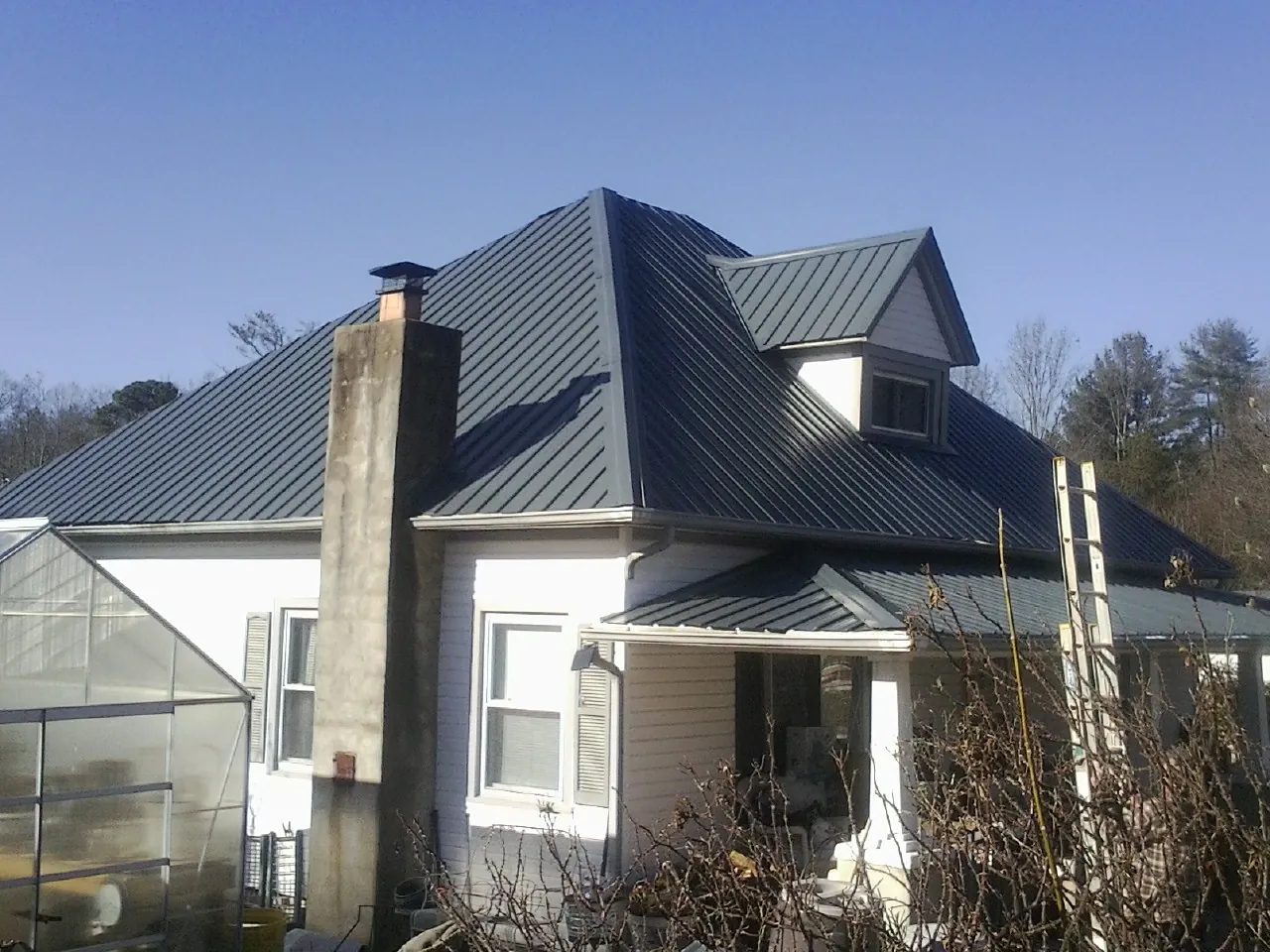 Dark blue standing seam metal roof on a white farmhouse with dormer — Slate & Tile Roof Repair by Roofing Brothers in Beulaville