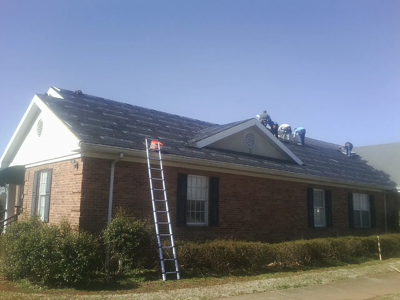 Crew tearing shingles off a brick ranch roof with a ladder set — Emergency Roof Repair work by our crew in Beulaville