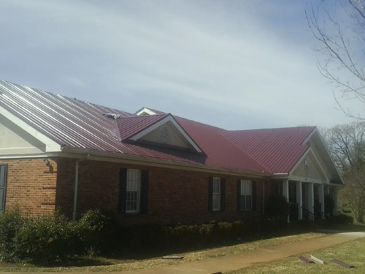 Red metal roof with gabled entries on a long brick building, from a Hail Damage Roof Repair job in Beulaville