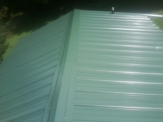 New green metal panels meeting at the ridge of a roof — Flat Roof Repair work by our crew in Beulaville