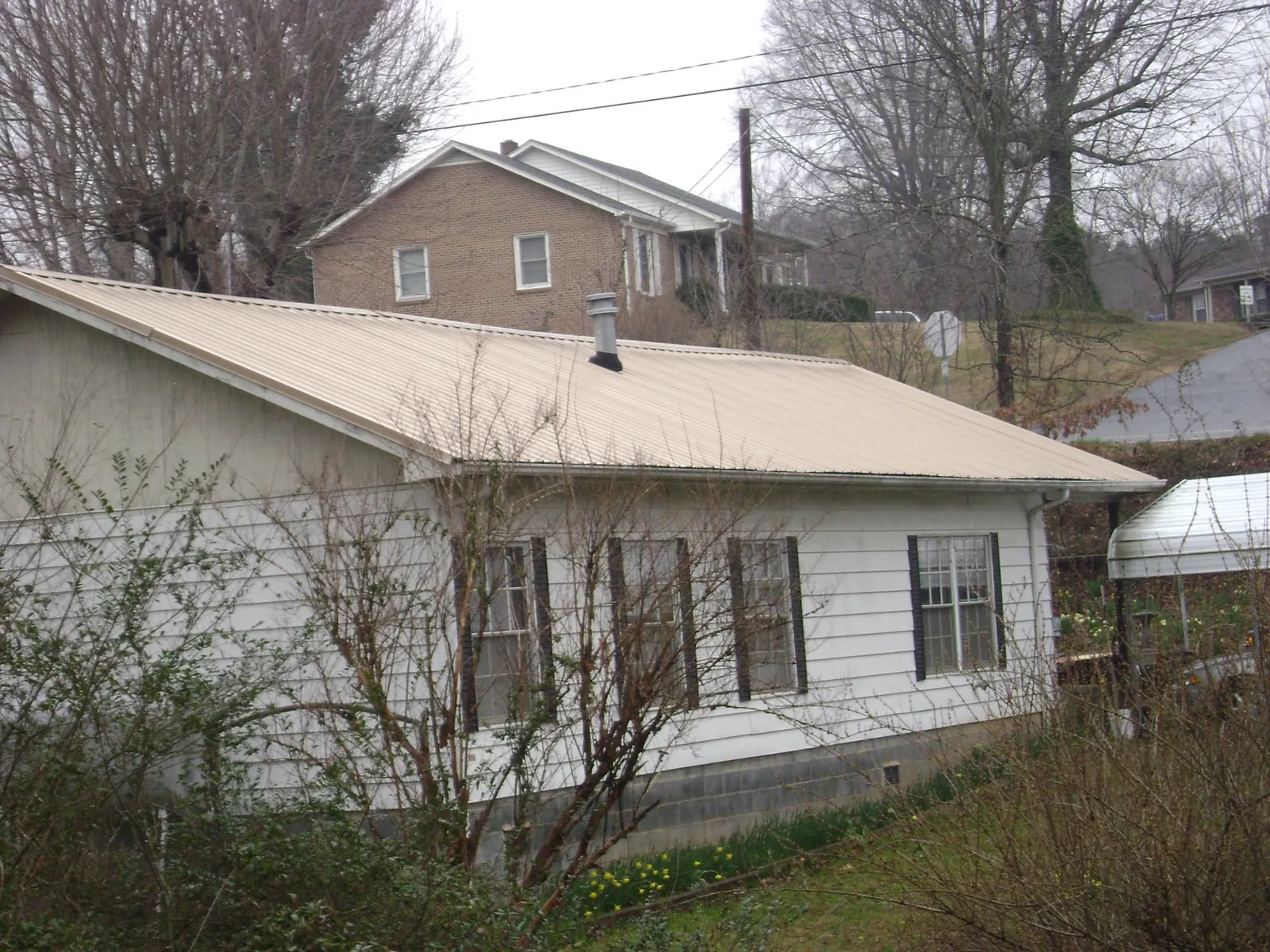 Tan metal roof on a white sided house set into a hillside — Commercial Roofing by Roofing Brothers in Beulaville
