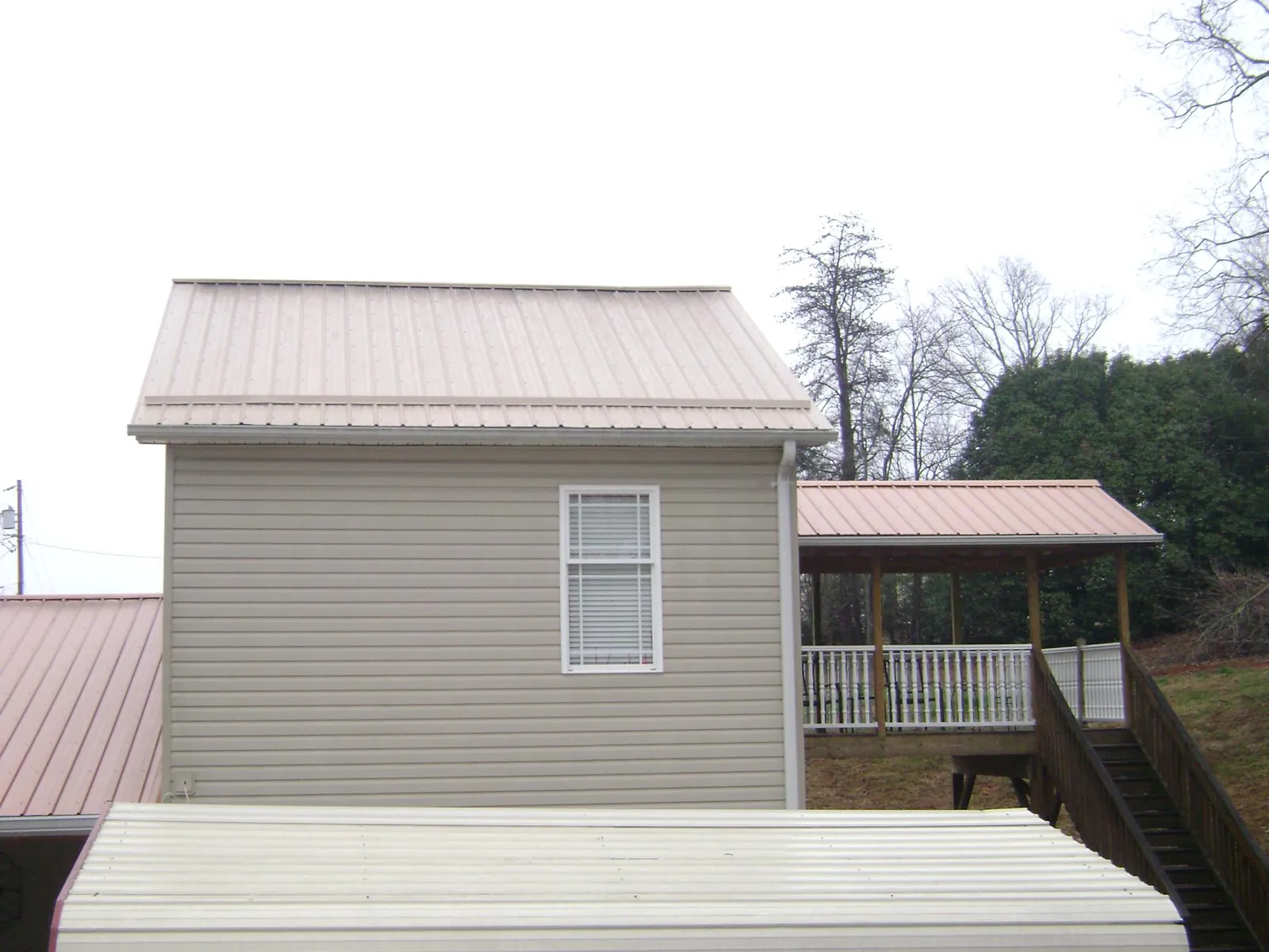 Tan metal roofs on a two story addition and attached porch, from a Roof Replacement job in Beulaville